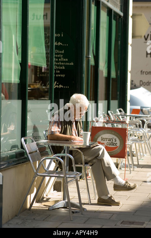 middle aged man by himself reading book sitting outside a  Coffee bar Aberystwyth Ceredigion wales UK Stock Photo