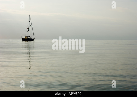 a sailing boat yacht at dusk over cardigan bay calm sea Aberystwyth Ceredigion Wales UK Stock Photo