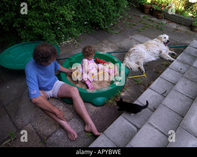 Family in Sandpit Grandfather with Two Year Old Granddaughter wearing Wellington Boots in Sandpit Stock Photo