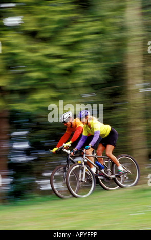 A couple riding mountain bikes speed down a hill in a forest Stock Photo