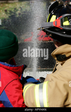 A Mequon Fire Department Firefighter and a young boy using a hoseline to spray water on a house fire demonstration Stock Photo