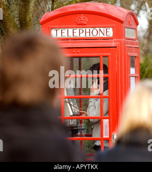 A young man using a red telephone box in a busy urban street. Picture by Jim Holden. Stock Photo