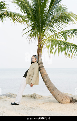 Young man leaning against palm tree. Stock Photo