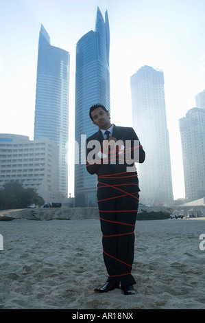 Businessman tied with rope, towers seen through the mist in the background Stock Photo