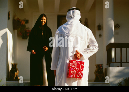 Rear view of a husband hiding a gift from his wife. Stock Photo
