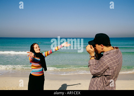 A man takes a photograph of the woman on the beach. Stock Photo