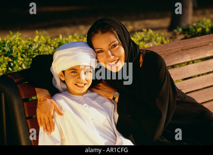 A mother and a son smiles at the camera as they rest on the bench. Stock Photo