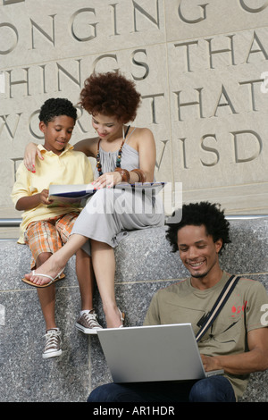 african american family entertaining, mother and son, boy reading book and father on laptop Stock Photo