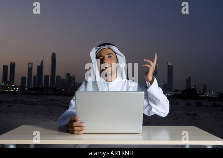 Young Arab man sitting at a desk  - office with Dubai City in the background Stock Photo