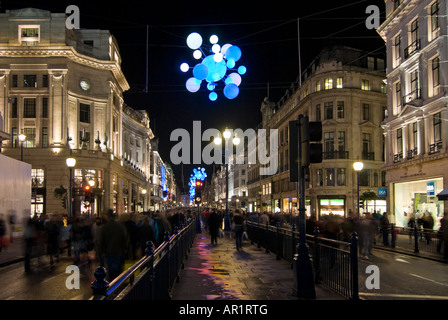 Horizontal wide angle of the colourful Christmas lights and lots of shoppers walking along Regent Street in the rain at night Stock Photo