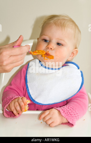 Vertical close up of a pretty Caucasian baby girl sitting at her high chair at dinner time getting in a mess Stock Photo
