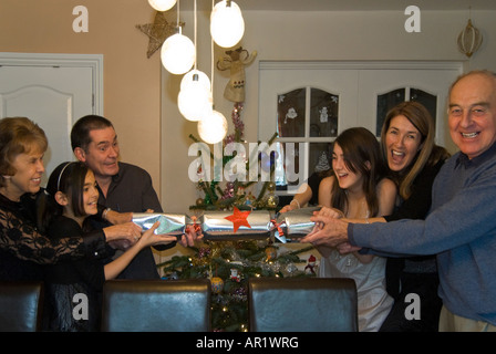 Horizontal portrait of three generations of a family, grandparents parents and children pulling a giant cracker on Christmas day Stock Photo