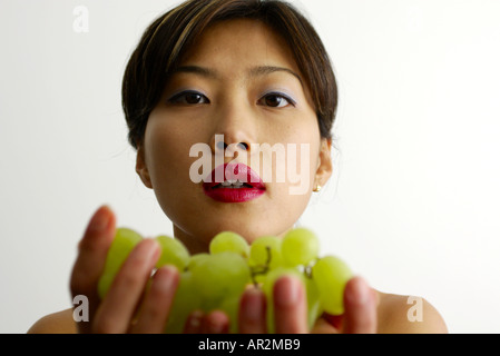 portrait of beautiful young oriental female with red lips holding bunch of green grapes Stock Photo