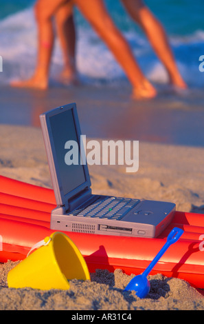 Beach toys and laptop computer on beach with couple walking in the background Miami Florida USA Stock Photo