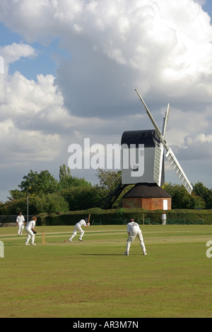 Iconic quintessential England idyllic village green cricket match bowler batsman & fielders Mountnessing Post Mill beyond in Essex countryside UK Stock Photo