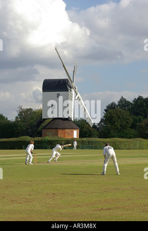 Iconic quintessential England idyllic village green cricket match bowler batsman & fielders Mountnessing Post Mill beyond in Essex countryside UK Stock Photo