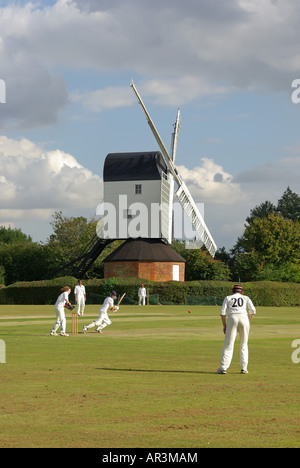 Iconic quintessential England idyllic village green cricket match bowler batsman & fielders Mountnessing Post Mill beyond in Essex countryside UK Stock Photo