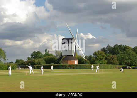 Iconic quintessential England idyllic village green cricket match bowler batsman & fielders Mountnessing Post Mill beyond in Essex countryside UK Stock Photo