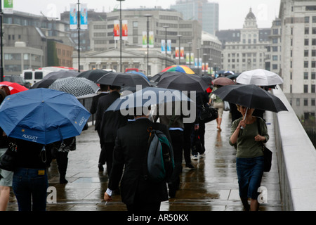Commuters crossing London Bridge during rain-sodden morning rush hour, London Stock Photo