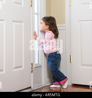 Caucasian girl toddler peeking out of window by door Stock Photo