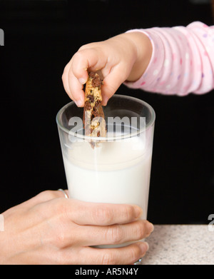 Caucasian girl dipping chocolate chip cookie into glass of milk Stock Photo