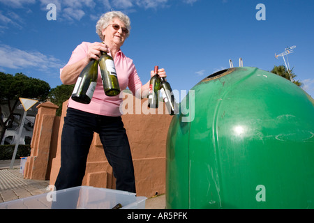 Senior woman throwing glass bottles into recycle bin Stock Photo