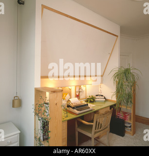 Lighting above typewriter on wooden desk below concealed bed in seventies homeoffice with houseplants on pine shelves Stock Photo