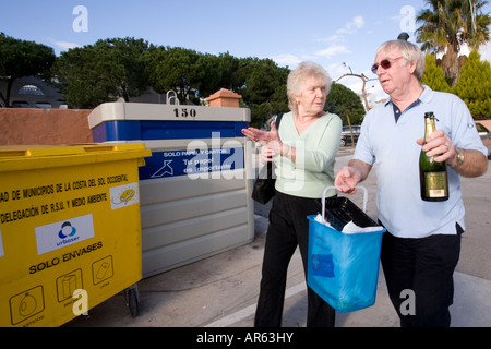 Senior couple throwing glass bottles into recycle bin Stock Photo