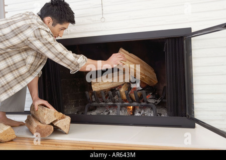 Asian man putting logs in fireplace Stock Photo