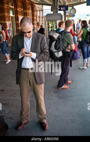 Business commuter using PDA on train station platform waiting for train to arrive Stock Photo