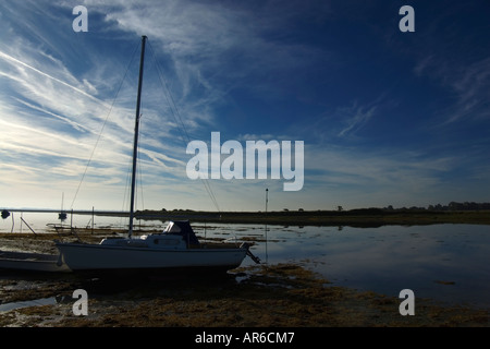 a small sailing yacht aground at low tide in a calm backwater at sunrise on Hayling Island in Hampshire England UK Stock Photo