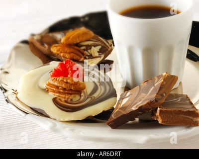 white, plain and milk chocolate marbled swirl with fresh strawberries and pecan nuts on a tray with black coffee. Stock Photo