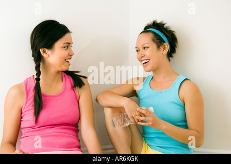 Two young women in fitness clothes sitting smiling and talking Stock Photo