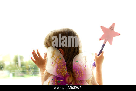 4 year old female child dressed as fairy with wand, looking out window Stock Photo
