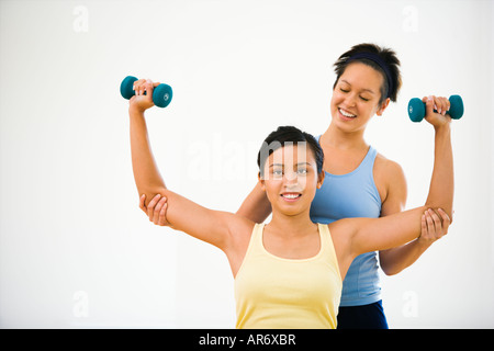 Young woman lifting hand weights while another woman helps position her arms Stock Photo