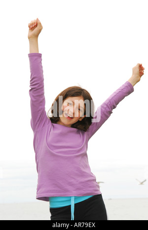 Portrait of a young girl on sea shore with arms raised in excitement Stock Photo