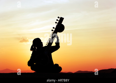 Indian man playing a sitar on rock at sunset. India Stock Photo