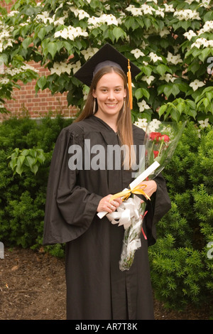 A young woman in cap and gown stands proudly with her diploma on graduation day. Stock Photo