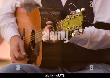 Close-up image of a man strumming on a guitar as he holds it on his lap. Stock Photo