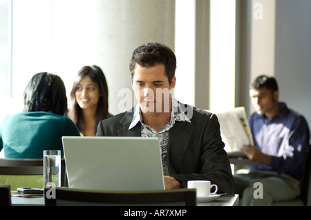 Young urban business man using laptop in busy cafe. Stock Photo