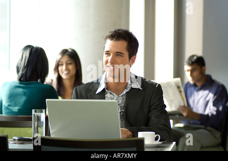 Young urban business man using laptop in busy cafe. Stock Photo