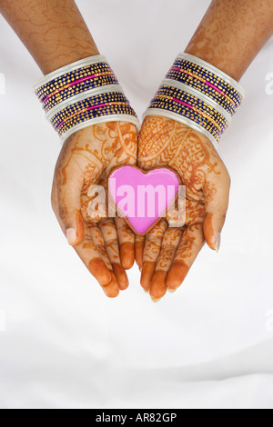 Indian girl with henna hands holding pink heart shaped dish. India Stock Photo