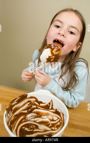 Little girl licking chocolate from bowl off spoon after baking Stock Photo