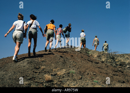 A group of seven white women tourists stride up a ridge following their Guide to look for fossils in Sibiloi National Park Kenya Stock Photo