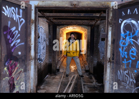 Man standing in the tunnel of an abandoned brick factory oven with graffiti on doors Don Valley brickworks Toronto Stock Photo