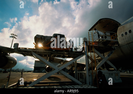 Boeing 747 jumbo jet un loading cargo freight containers pallets against a cloudy sky men airport workers silhouette Stock Photo