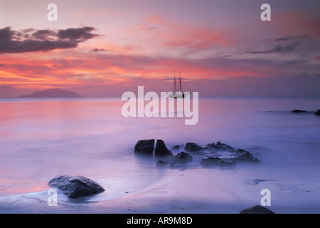 Old masted ship anchored in Indian Ocean off Seychelles at sunset Stock Photo