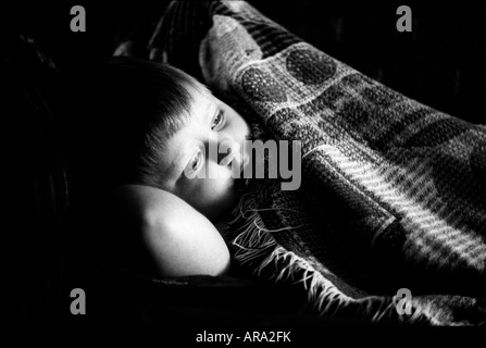 Young boy rests on couch under patterned blanket with his arm behind his head. Stock Photo