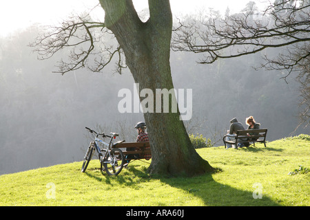 A couple sitting on a park bench looking across the Avon Gorge by Brunel's historic Suspension bridge in Clifton Bristol U.K. Stock Photo