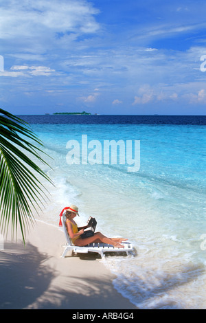 Woman sitting on sandy shore on beach chair with laptop during working holiday Stock Photo